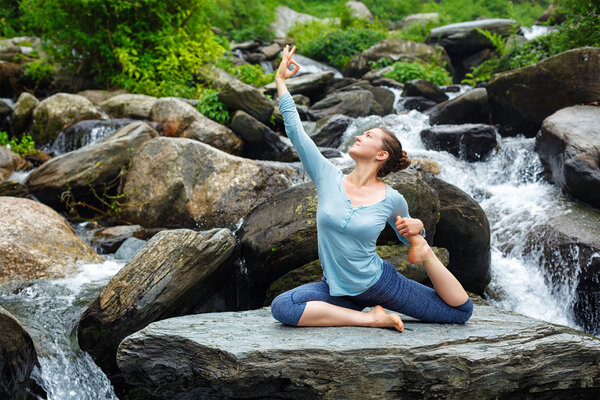 Woman doing yoga outdoors at tropical waterfall