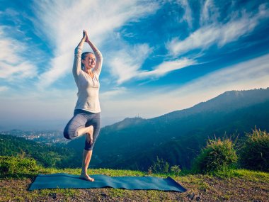 Woman doing yoga asana Vrikshasana tree pose in mountains outdoors