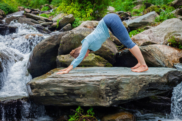 Young sporty fit woman doing yoga oudoors at tropical waterfall