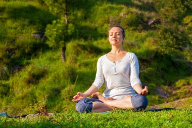 Genç, sportif, formda bir kadın dışarıda yoga yapıyor.