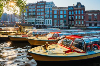 Günbatımında Amsterdam kanalı rıhtımında demirlemiş turist tekneleri
