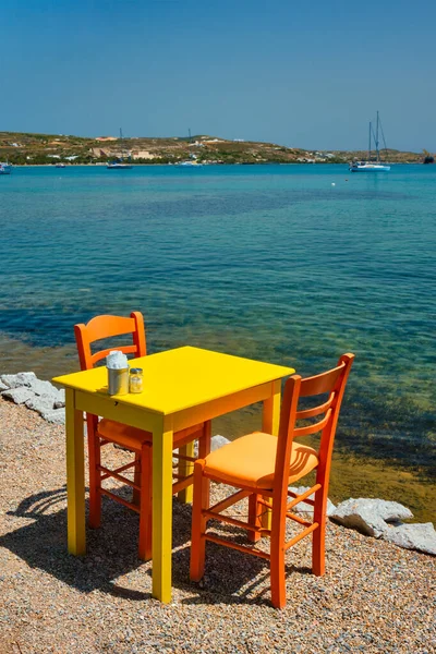 Café praia de mesa na cidade de Adamantas na ilha de Milos com mar Egeu com barcos no fundo — Fotografia de Stock