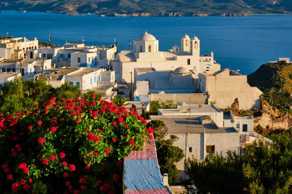 Picturesque scenic view of Greek town Plaka on Milos island over red geranium flowers — Stock Photo, Image