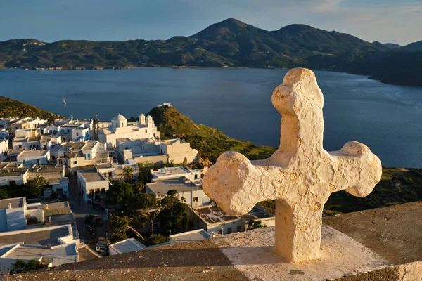 Croce cristiana e villaggio di Plaka sull'isola di Milos su fiori di geranio rosso al tramonto in Grecia — Foto Stock