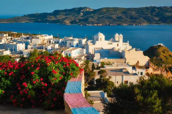 Picturesque scenic view of Greek town Plaka on Milos island over red geranium flowers — Stock Photo, Image