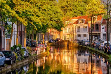 Gün batımında parkedilmiş eski evler ve arabalarla dolu delta kanalı.