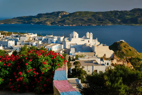 Schilderachtig uitzicht op de Griekse stad Plaka op het eiland Milos over rode geranium bloemen — Stockfoto