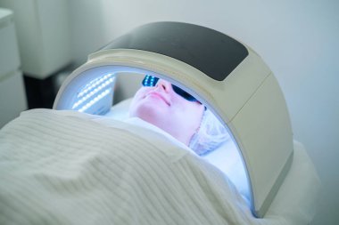 Bir kadın sivilceleri hedef almak ve kaplıcalarda cilt berraklığını artırmak için LED ışık terapisi ile yüz temizleme seansı alır..