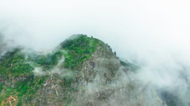 Bir dron Miradouro Eira do Serrado, Madeira, Portekiz 'in dağlarını görüntüler. Bulutlar tepeleri sarıyor. Ağaçlar ve dik kayalık oluşumlar görülebilir..