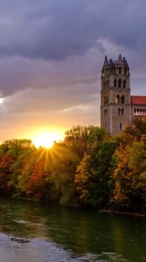 Münih 'in dramatik günbatımında zaman aşımı: ünlü turistik Bavyera şehrinde sonbahar. Reichenbach Köprüsü 'nden Isar nehri, ağaçlar ve kilise manzarası. Munchen, Bavyera, Almanya. Kamera yakınlaştır