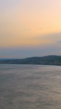 Nice, Fransa 'nın gün batımındaki manzarası. Akdeniz dalgaları sahilde dalgalanır, insanlar sahilde dinlenir, arabalar yolda ilerler. Güzel, France. Kamera yatay tavası