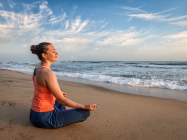 Young sporty fit woman doing yoga oudoors at beach clipart