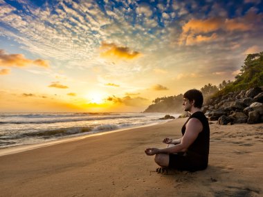 Young fit man do yoga meditation on tropical beach clipart