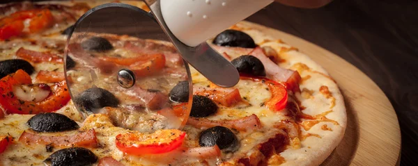 Pizzaschneiderrad schneidet Schinken-Pizza — Stockfoto