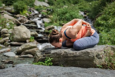 Young woman does yoga oudoors at waterfall