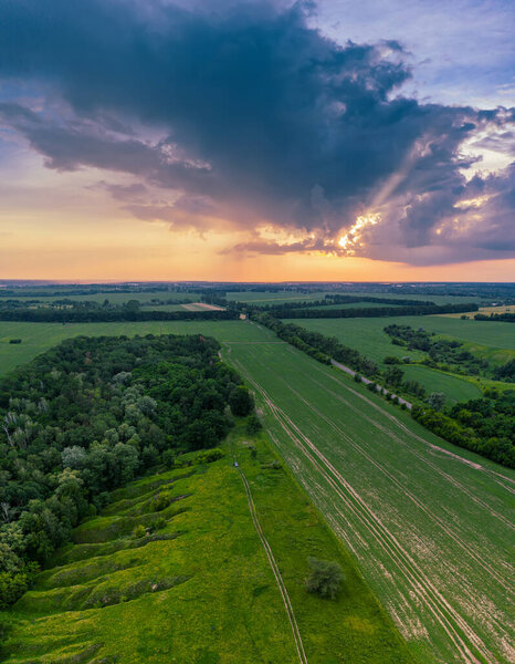 Rural summer sunset landscape with green fields and dramatic colorful sky, natural background, aerial view