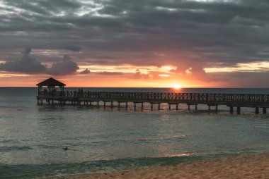 Dominik Cumhuriyeti 'ndeki güzel Karayip plajı. Mavi deniz suyu, renkli gökyüzü ve ahşap iskele ile tropikal cennet manzarası.