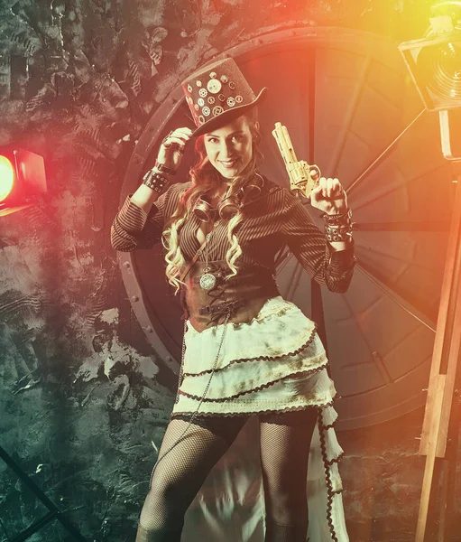 Steampunk woman with mechanical gun. Beautiful girl, model in the style of a steampunk in a beautiful creative studio. Fashion, style
