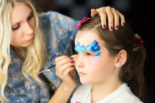 Woman painting the face of a little girl — Stock Photo, Image