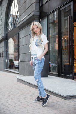 Pantolon ve tişört giymiş güzel bir kadın dükkanın yanında poz veriyor.