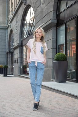 Pantolon ve tişört giymiş çekici bir kadın dükkânın yakınında poz veriyor.