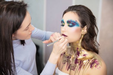 Sanatçı, stüdyodaki genç ve güzel bir modele makyaj yapar.
