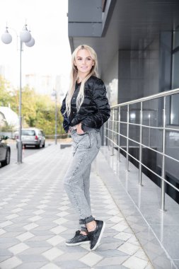 Korkulukların ve binanın yanında genç ve çekici bir sarışın duruyor.