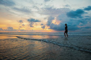 Endonezya 'nın Bali adasındaki Kuta plajında gün batımının arka planında bir kadının silueti.