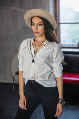 Stüdyoda pencere ve kanepenin yanında poz veren güzel bir kadın.