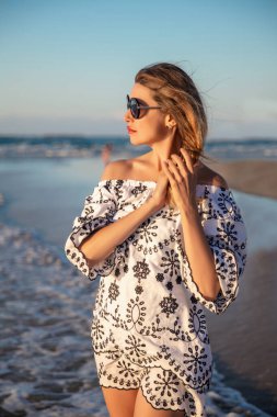 Akdeniz 'in arka planında beyaz bir tunikle süslenmiş güzel bir sarışının portresi.