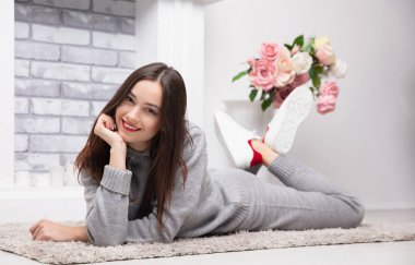 Gri takım elbiseli, şöminenin yanında poz veren hoş bir esmer kız.