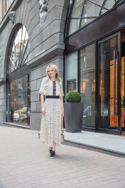 Binanın yanında poz veren uzun elbiseli güzel bir sarışın.