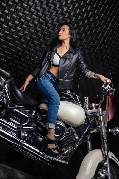 Nice young lady dressed in a leather jacket and jeans posing on a motorcycle