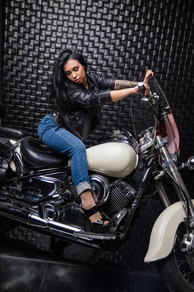 Nice lady dressed in a leather jacket and jeans posing on a motorcycle