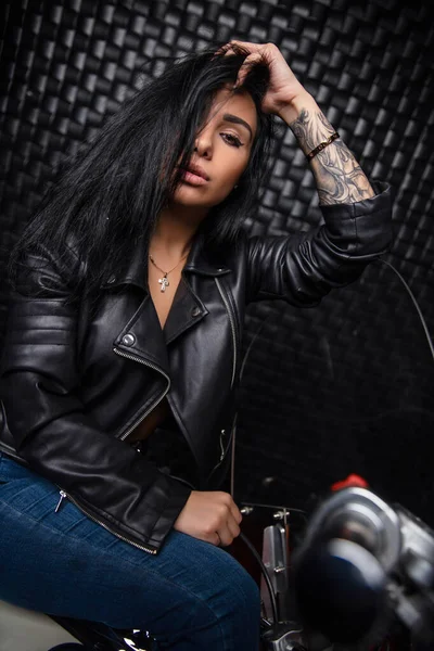 lovely lady dressed in a leather jacket and jeans posing on a motorcycle