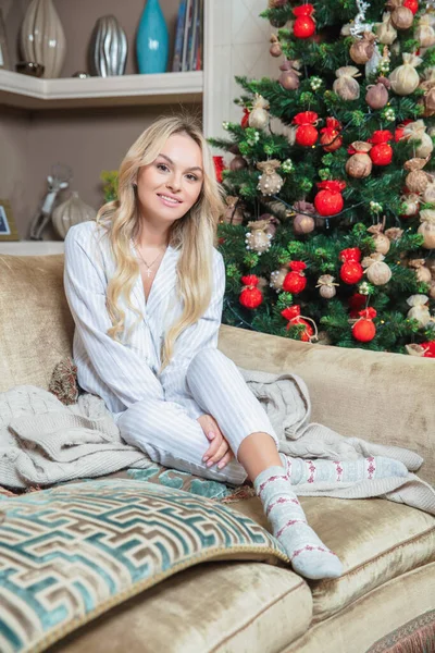 Cute Blondynka Ubrana Piżamę Pozowanie Podczas Siedzenia Kanapie Pobliżu Nowego — Zdjęcie stockowe