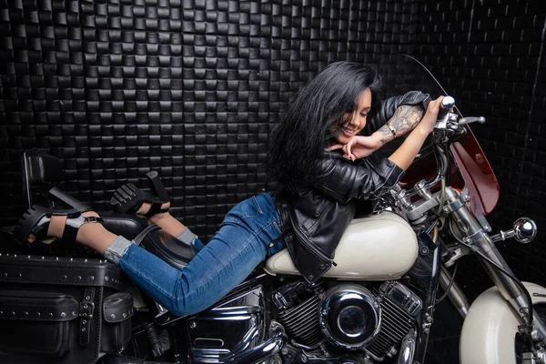 迷人的年轻女子穿着皮夹克 牛仔裤躺在摩托车上 — 图库照片