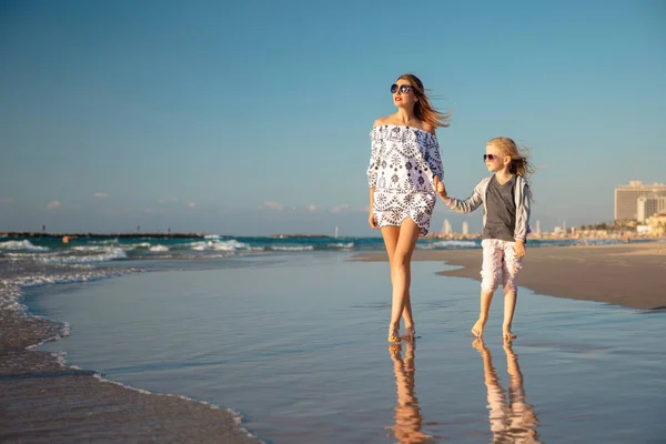 快乐的妈妈 带着一个小女儿赤脚在沙滩上冲浪 免版税图库照片