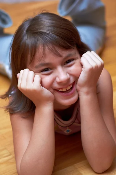 Sonriente chica acostada en el suelo apoyando su cabeza en las manos — Foto de Stock