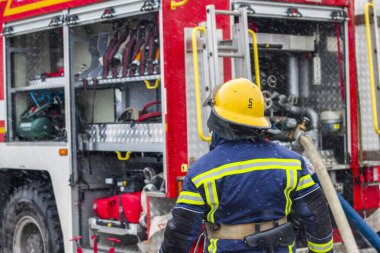 İtfaiye ekipmanı ve itfaiyeci. Kasklı ve üniformalı itfaiyeci aletlerle itfaiye aracına gider.