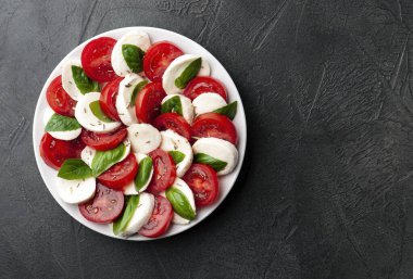 Domatesli İtalyan caprese salatası ve koyu arkaplanda fesleğen yapraklı mozzarella peyniri. Düz yatıyordu.