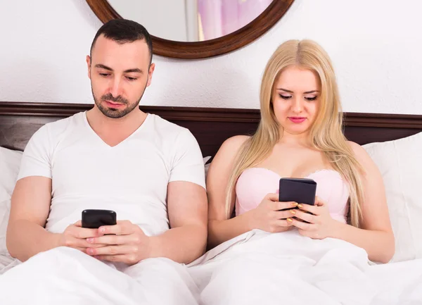 Casal com telefones na cama — Fotografia de Stock