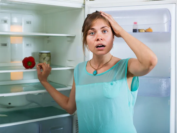 Järkyttynyt nainen katselee tyhjää jääkaappia — kuvapankkivalokuva