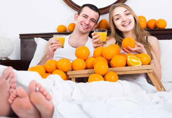 Man and girlfriend drinking squeezed orange juice in bed — Stock Photo, Image
