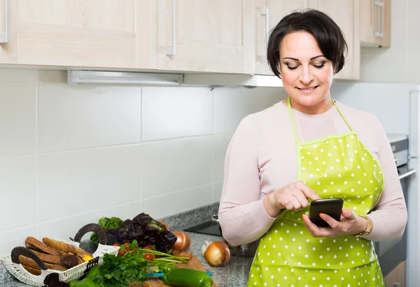 Huisvrouw in schort ontvangen van sms met recept — Stockfoto