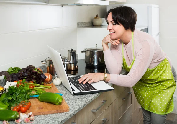 Dona de casa em avental com laptop na cozinha — Fotografia de Stock