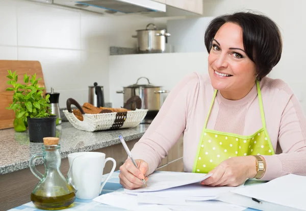 Ama de casa firmando papeles en la cocina — Foto de Stock
