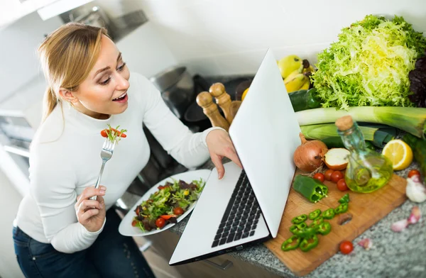 Mädchen isst mit Laptop in Küche — Stockfoto