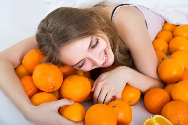 Portret van een meisje met sinaasappelen in bed — Stockfoto