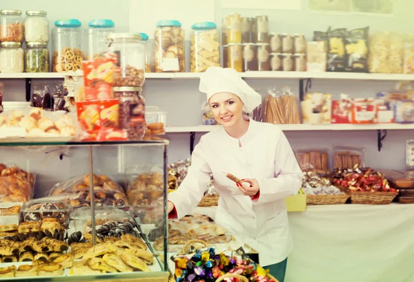Glückliche Verkäuferin bietet Süßigkeiten an Stockbild